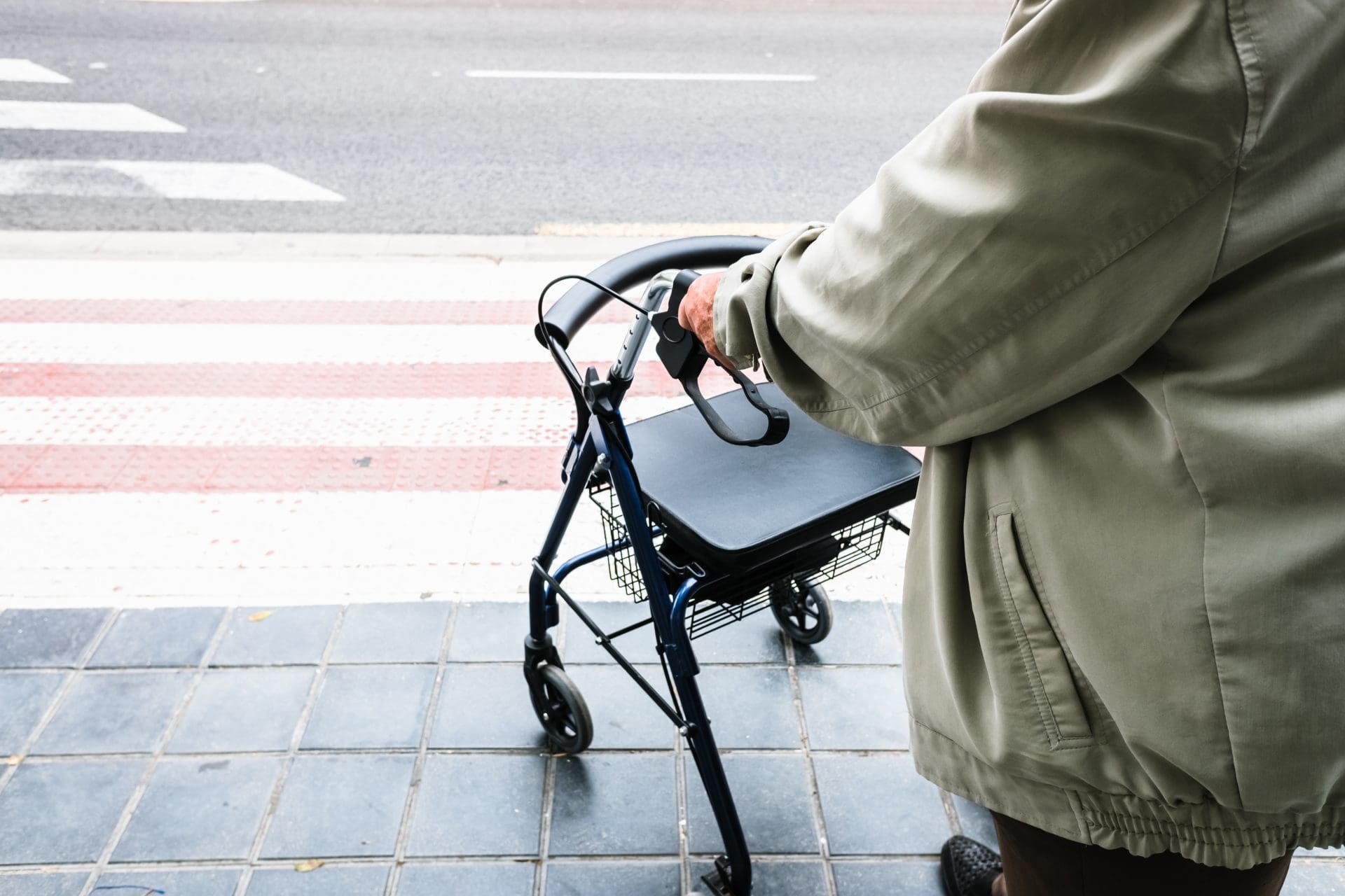 Elder waiting to cross a zebra crossing supported by a walker.