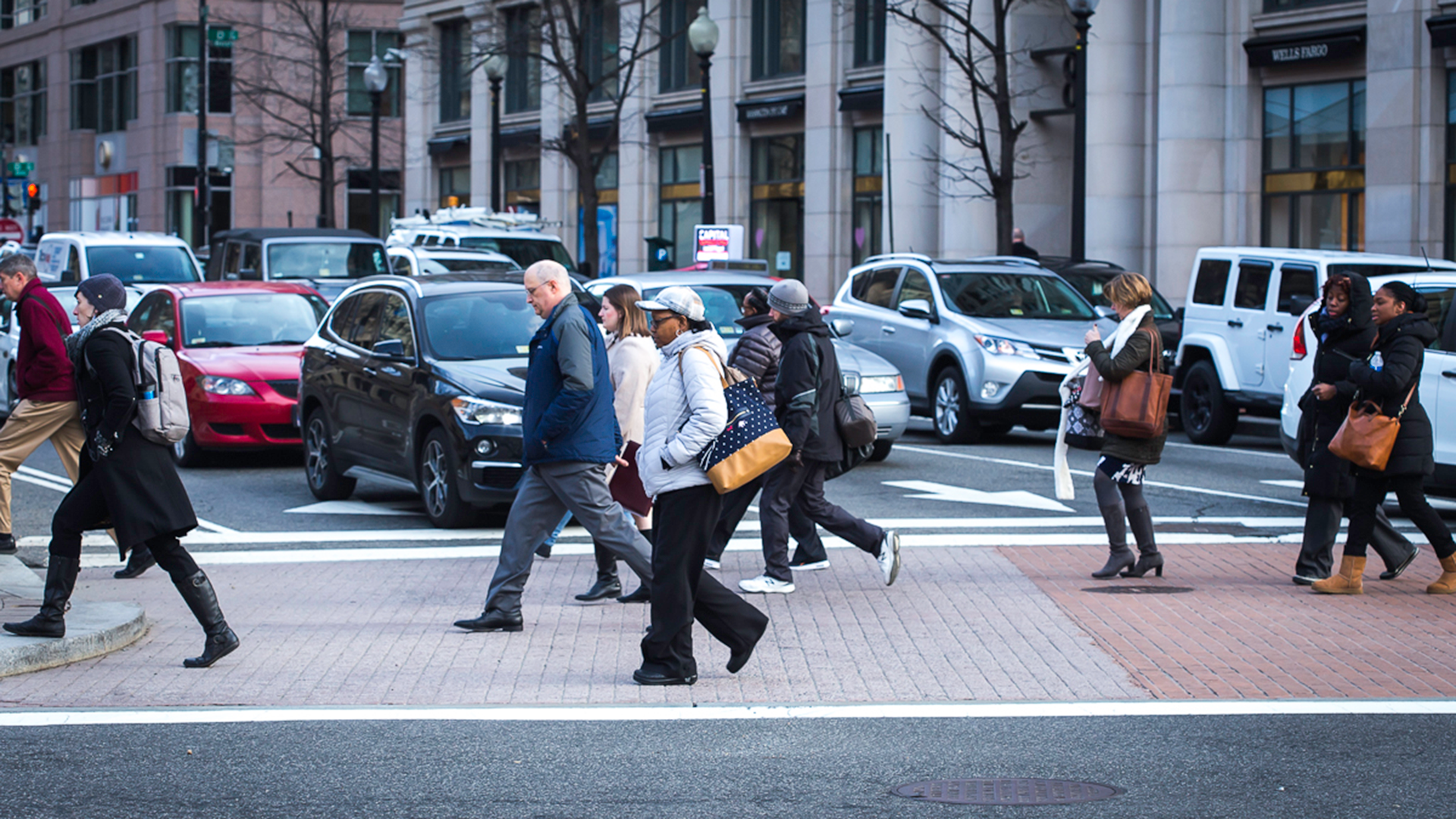 Pedestrians walking across the Penn Ave. crosswalk as cars wait.