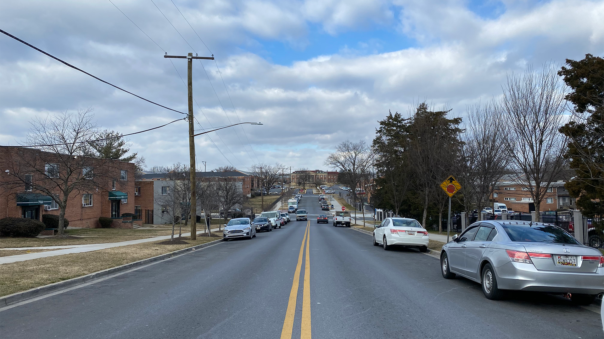 Street with cars parked on both sides, cloudy blue skies in background