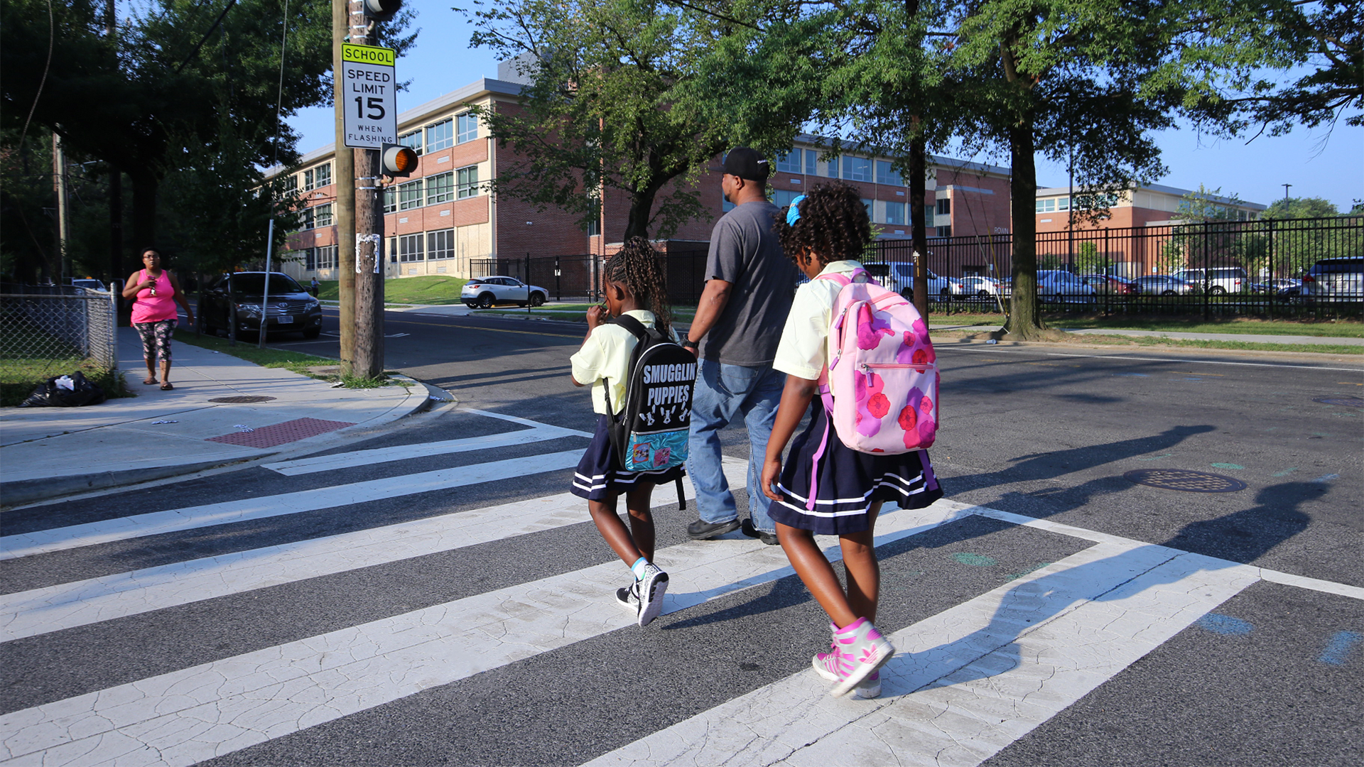 Parent walking two kids to school across a crosswalk.