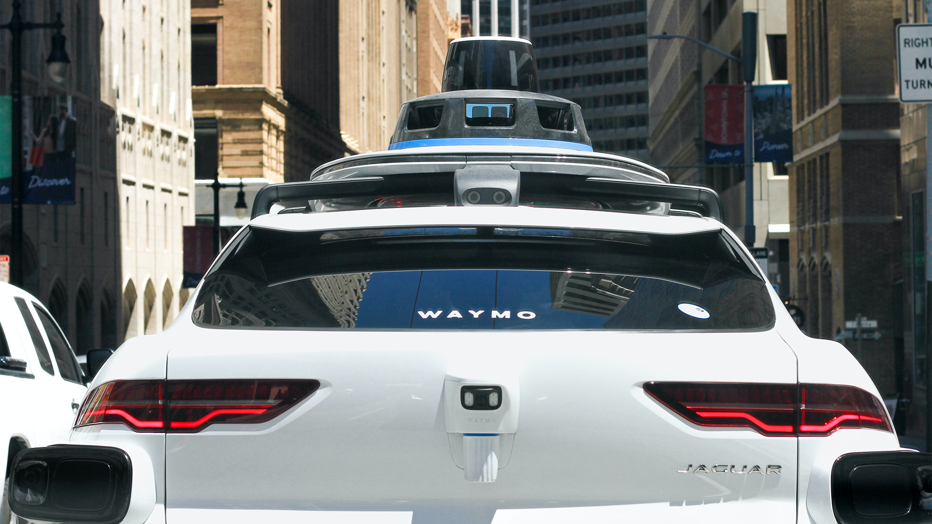 Back of a white Jaguar car with "Waymo" written on the back windshield.