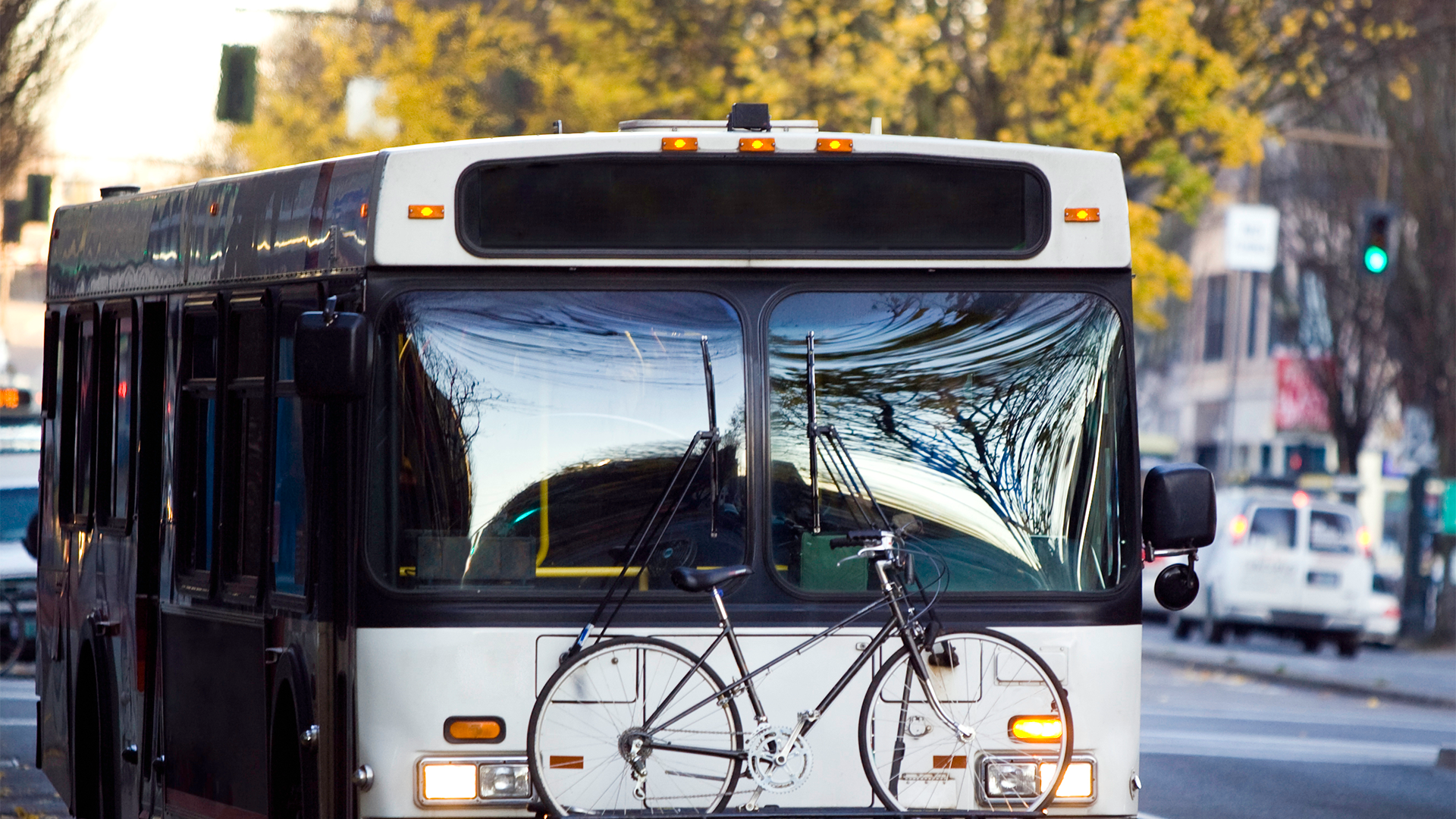 Bus with bike attached to front driving down the road in the daylight.