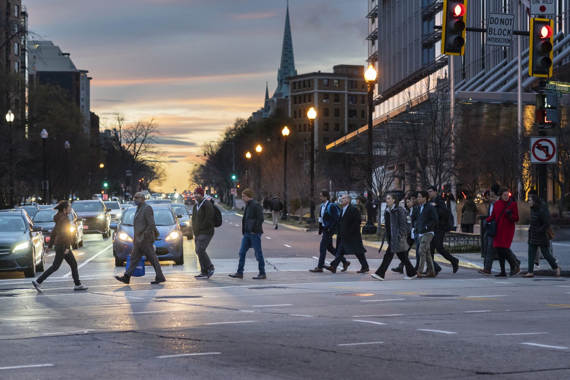 Group of people in business casual walking across crosswalk at dusk.