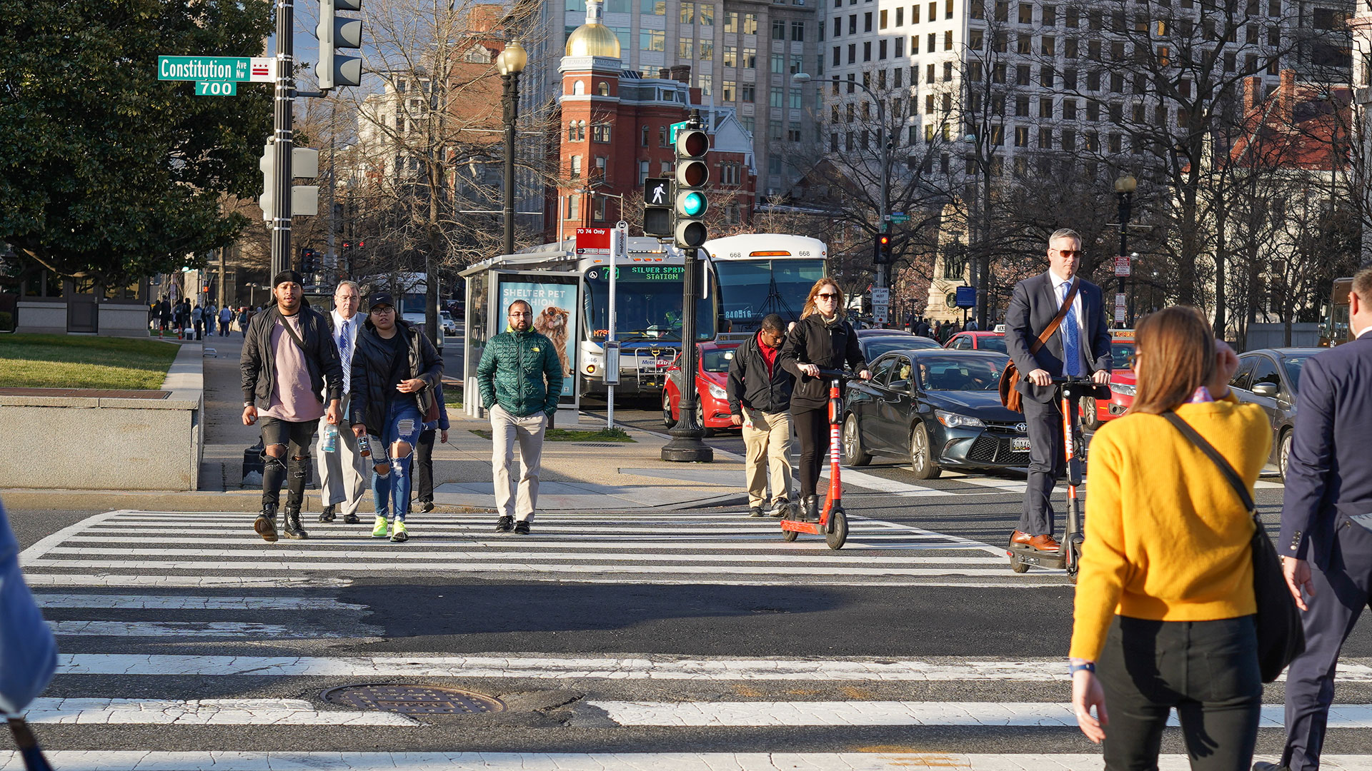 People on foot and scooter crossing a large sidewalk in a big city