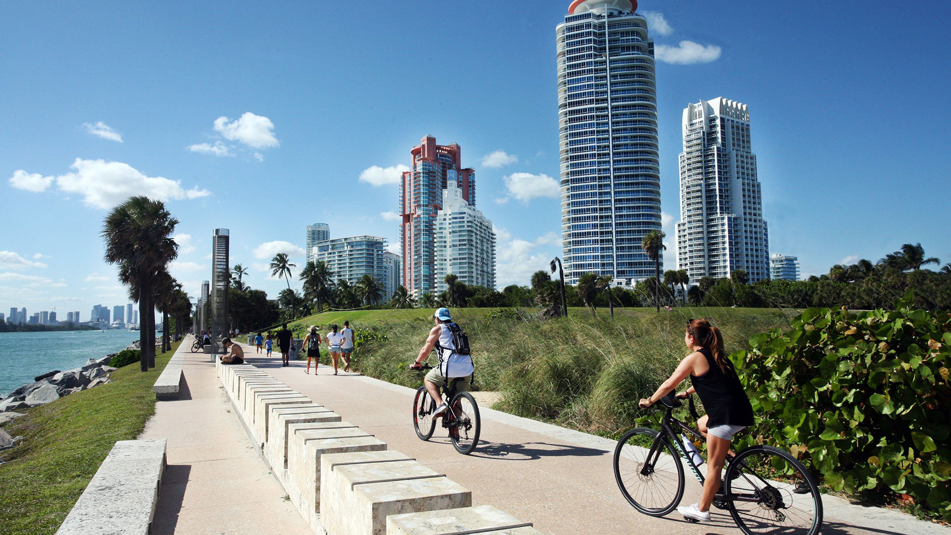 People riding bikes along a waterway with a city in the background