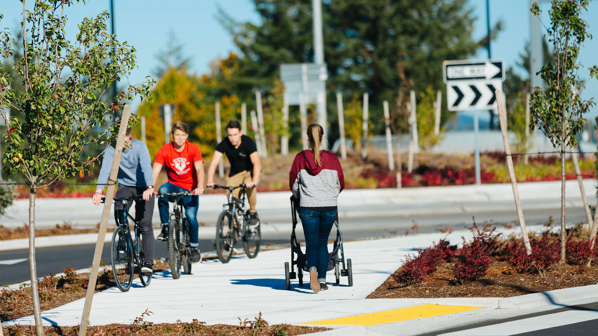 Person pushing a stroller and three people biking along a roundabout