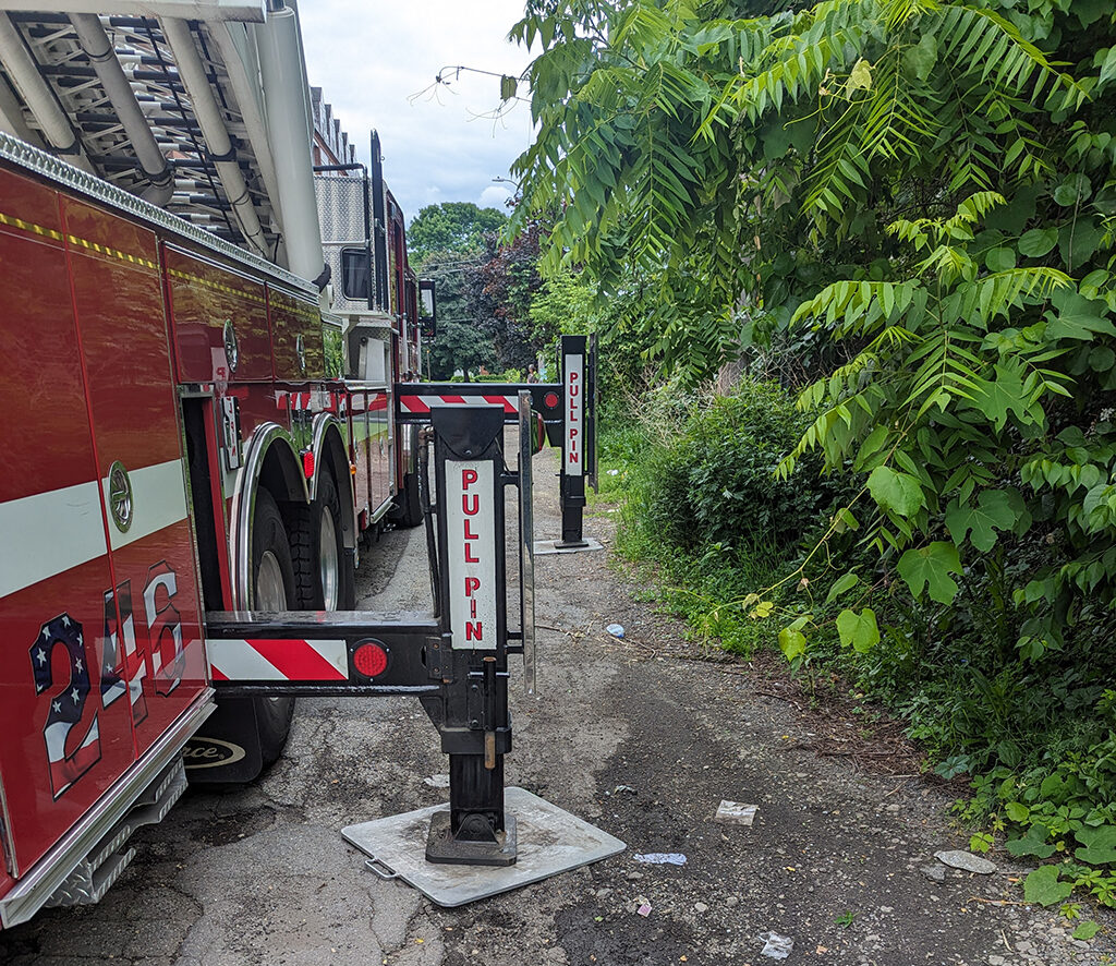 Two L-shaped arms reach out from the base of a fire truck and press into the ground to anchor the vehicle.