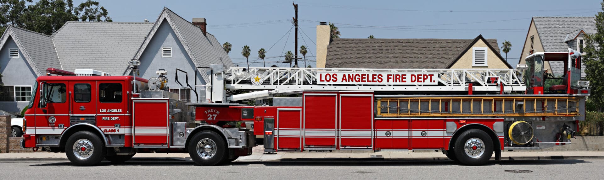 A long red tiller truck parked in front of multiple houses.