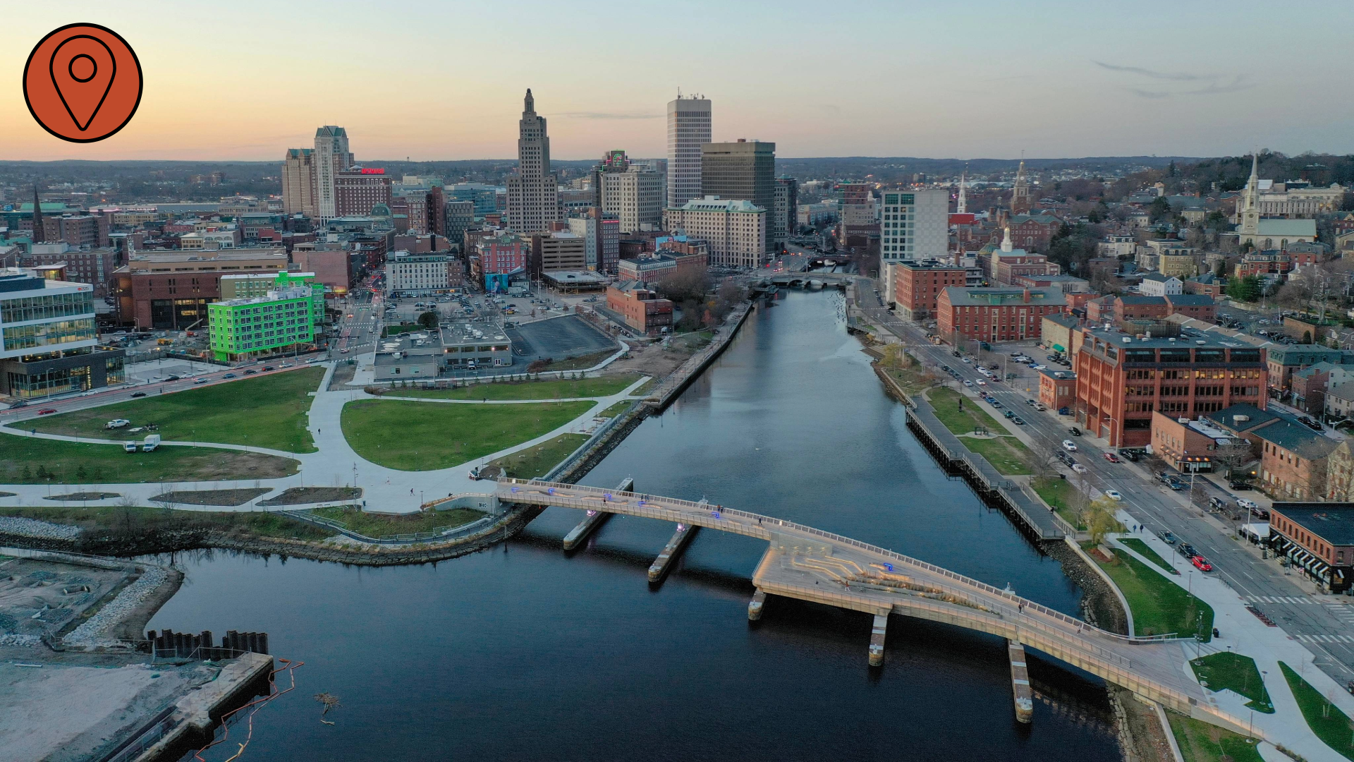 An aerial photograph of a bridge spanning two sides of an urban river. The bridge is exclusively intended for pedestrian use. A tiered platform for sitting and relaxing juts off of the bridge's main pathway.