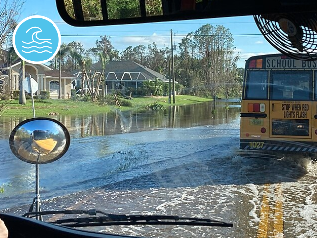 A school bus drives over partially flooded streets in a residential area.