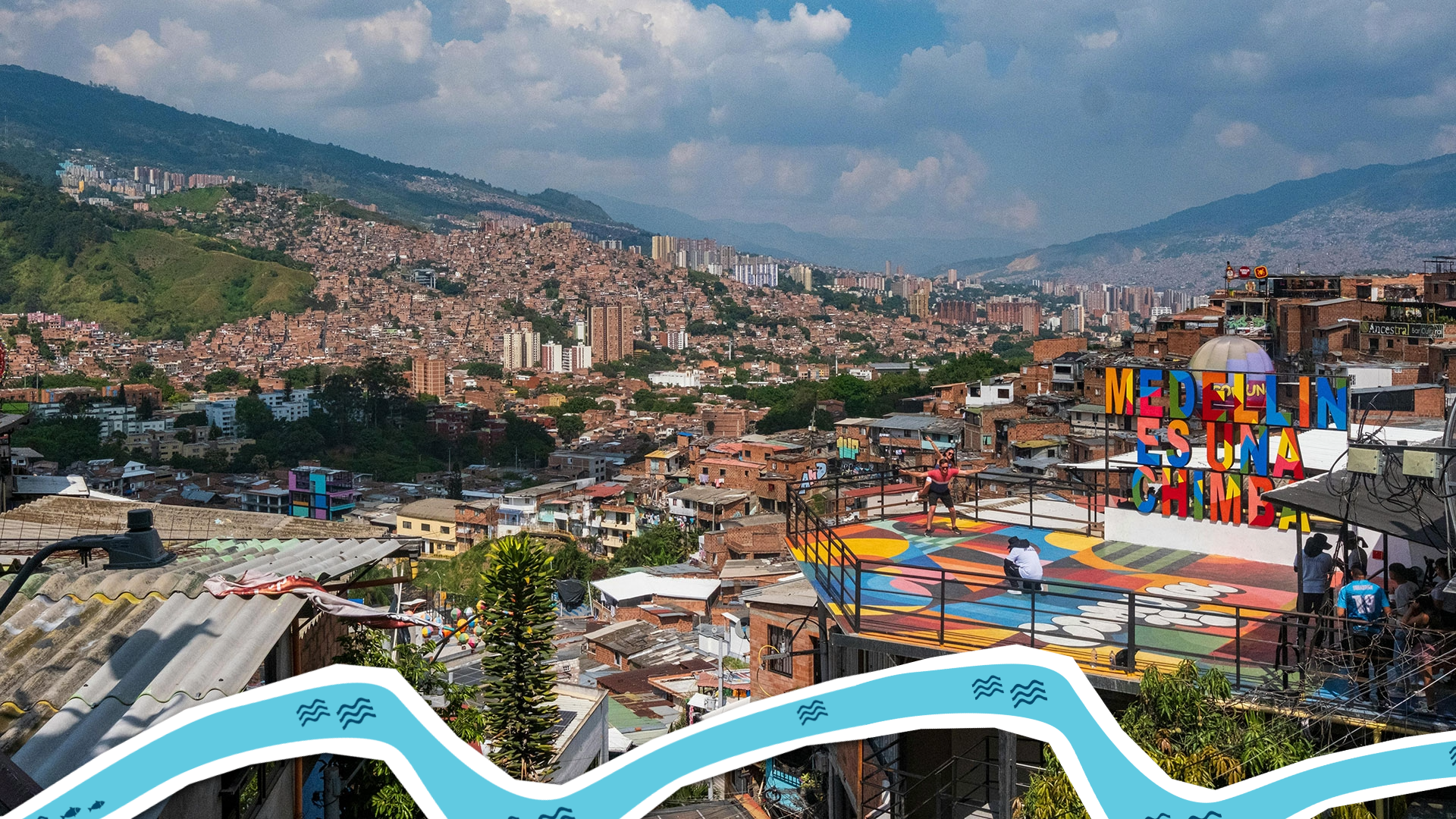 Photograph showing a colorful urban neighborhood in Medellín, Colombia, with densely packed houses extending up a hillside under a partly cloudy sky.