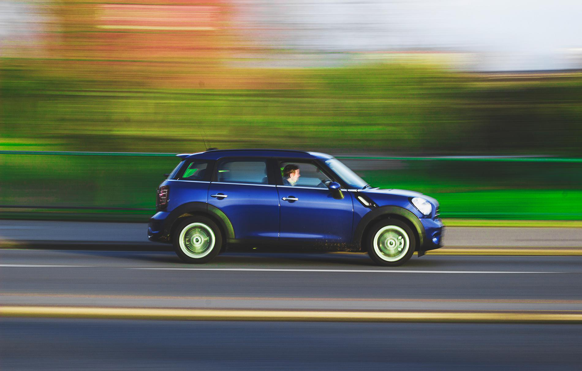 Photograph of a blue compact car driving on a multi-lane road with motion blur effect emphasizing speed.