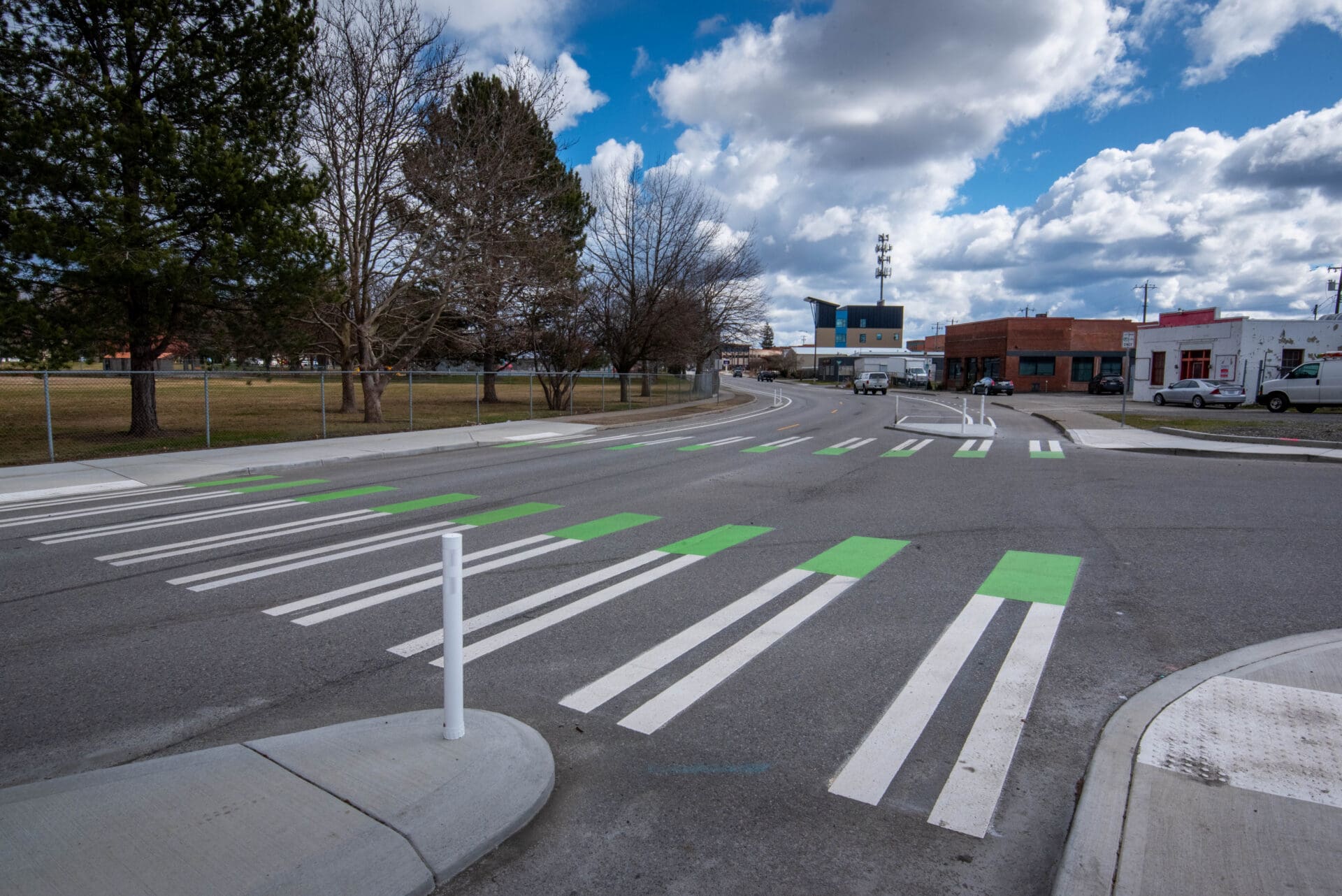 A street-level photo of an intersection with striped crosswalks and a dedicated bicycle lane running along the righthand side of the through lane. The bicycle lane and car lanes are separated at the intersection head by concrete bulb-outs.