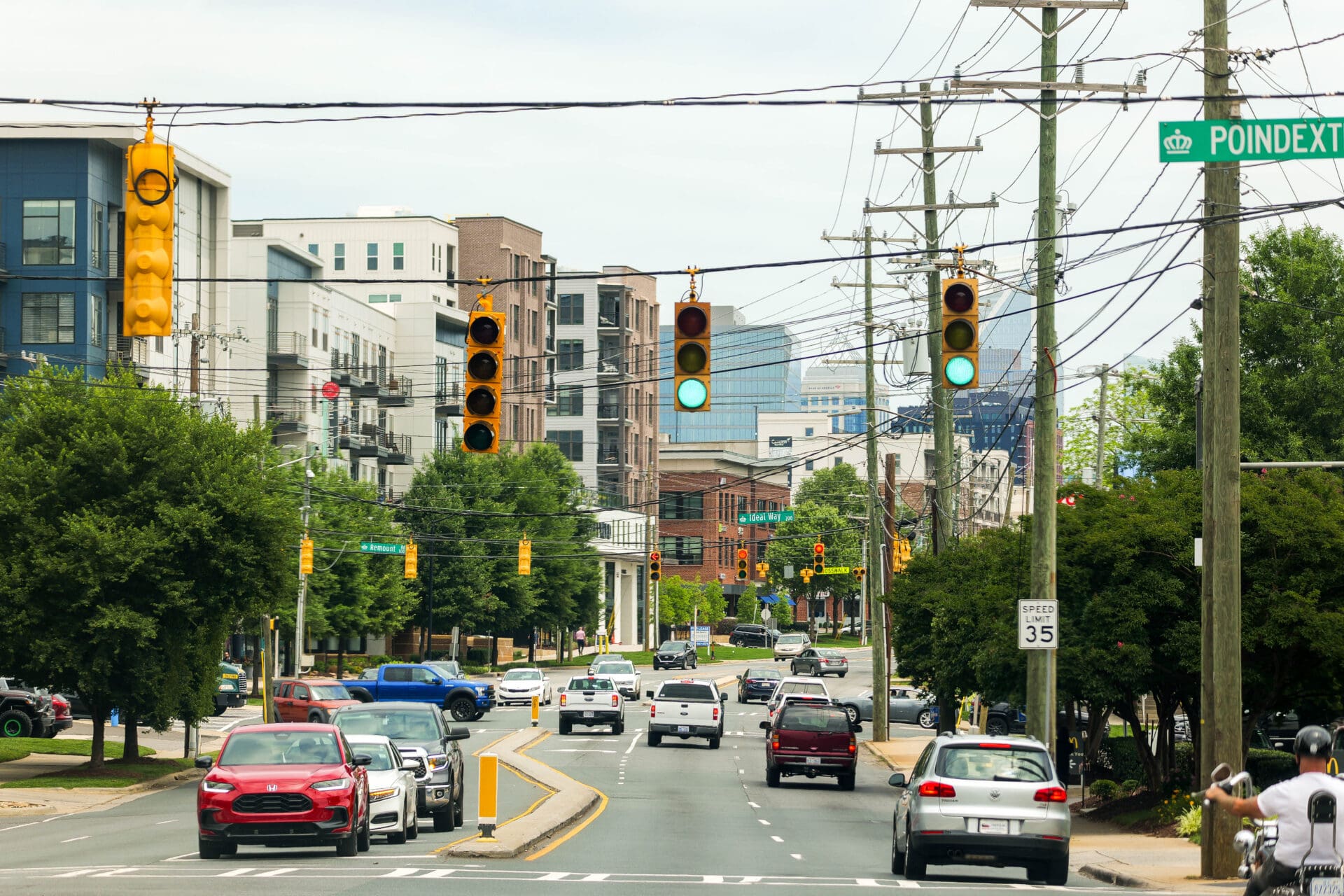 Photograph of an urban street intersection with multiple traffic lights showing green signals and various vehicles traveling in both directions.