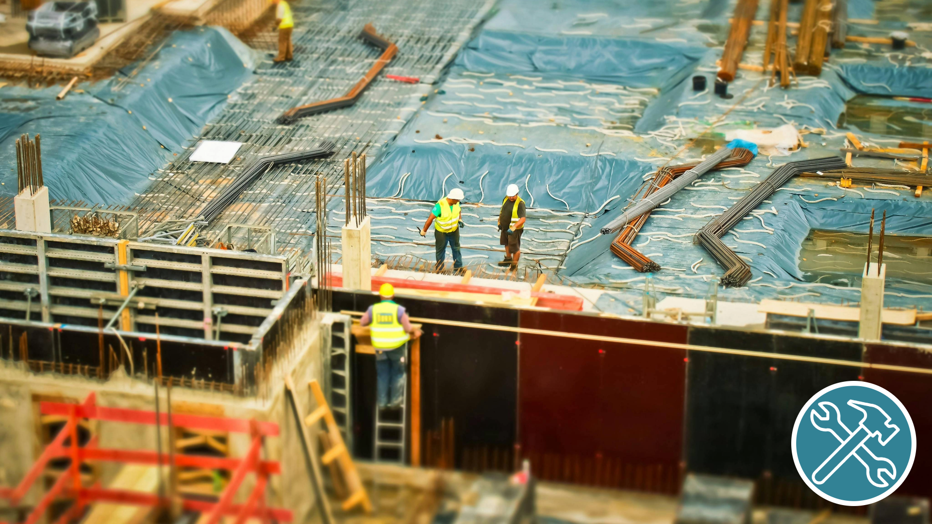 Construction site showing workers in safety vests and helmets amidst concrete forms, rebar, and wooden planks.