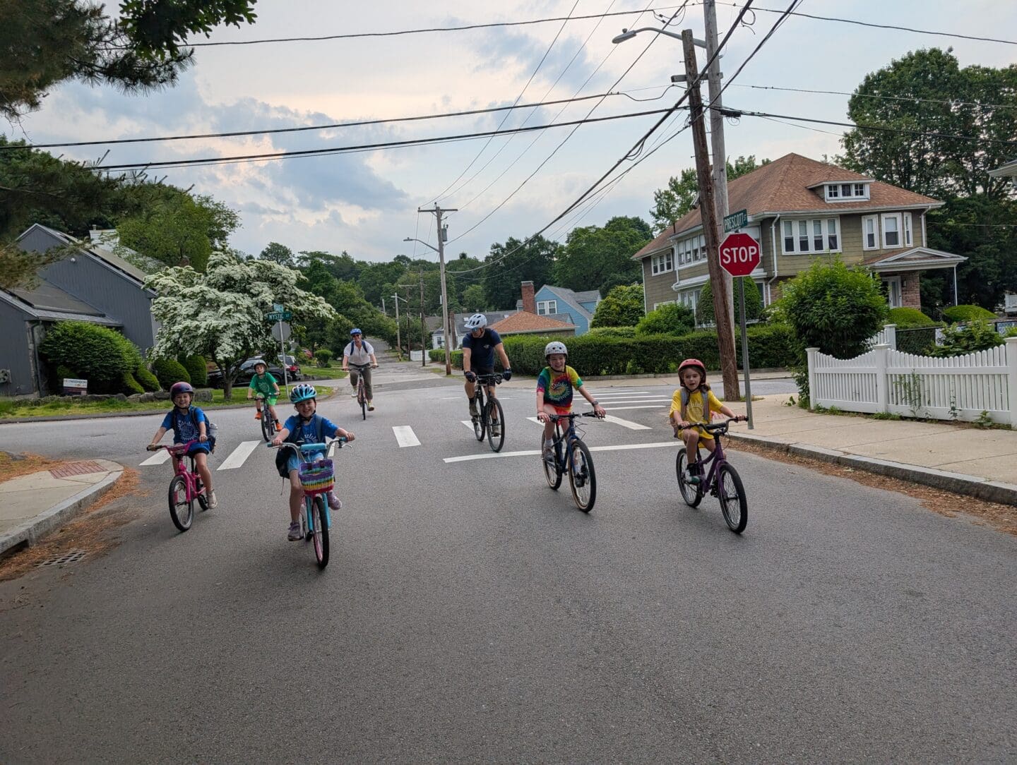 A group of children and two adults ride bikes in the middle of a residential street.