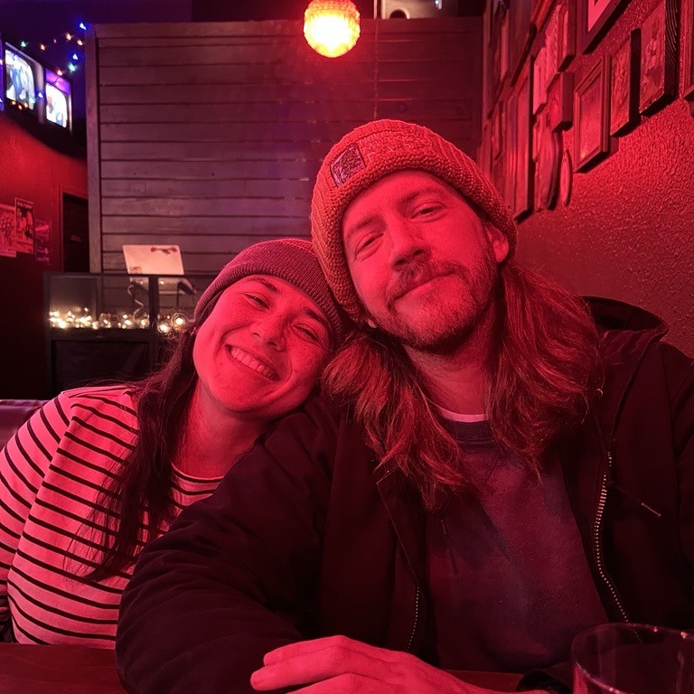 a selfie of a couple smiling in red lighting