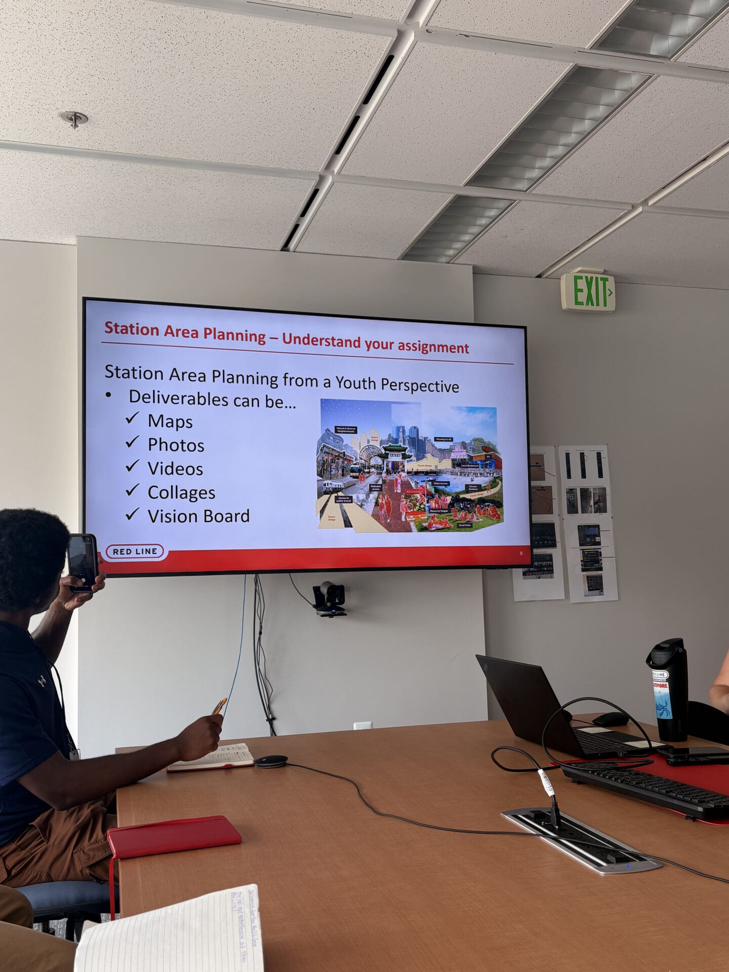 Photograph of a presentation slide displayed on a screen in a meeting room, that reads 