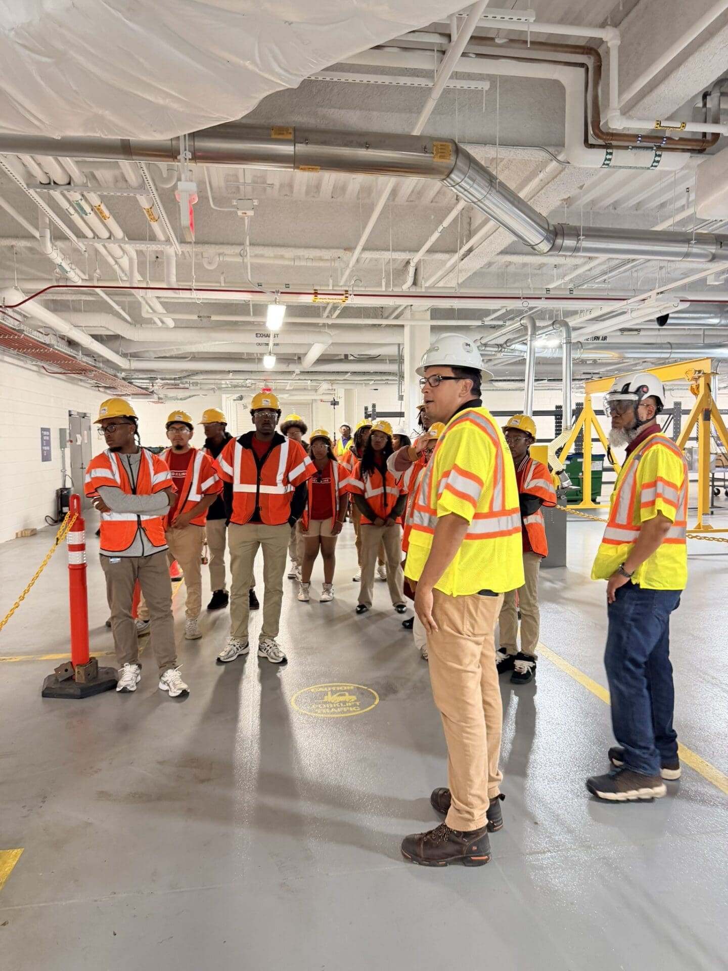 Photograph of a group of people wearing safety vests and hard hats inside an industrial or construction facility.