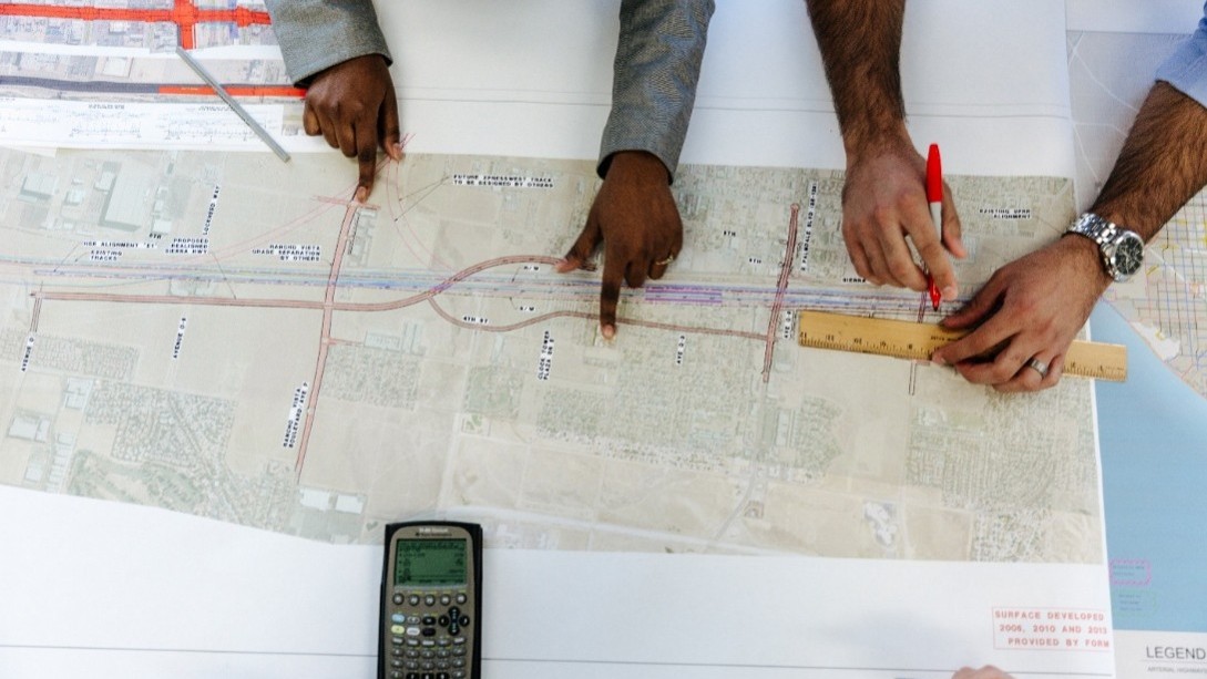 Hands point out and measure different sections of a road sketched onto a detailed map.