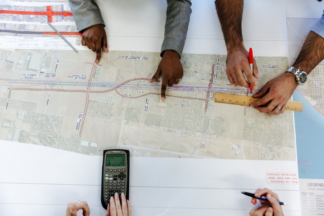 Hands point out and measure different sections of a road sketched onto a detailed map.
