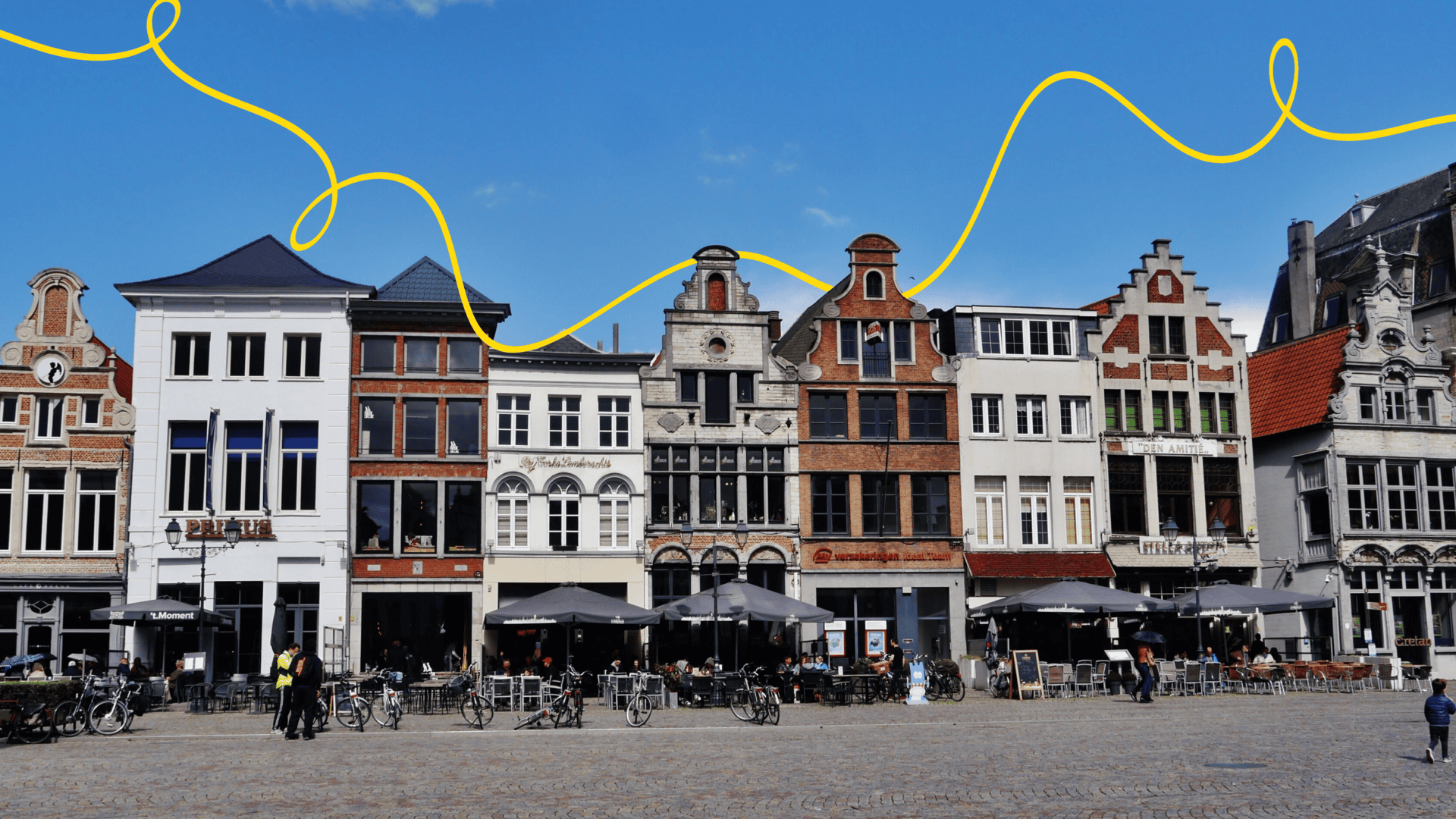 Image of Belgium's Grote Market. With European style buildings close together against a blue sky. There are tables with umbrellas and people lingering in the foreground.