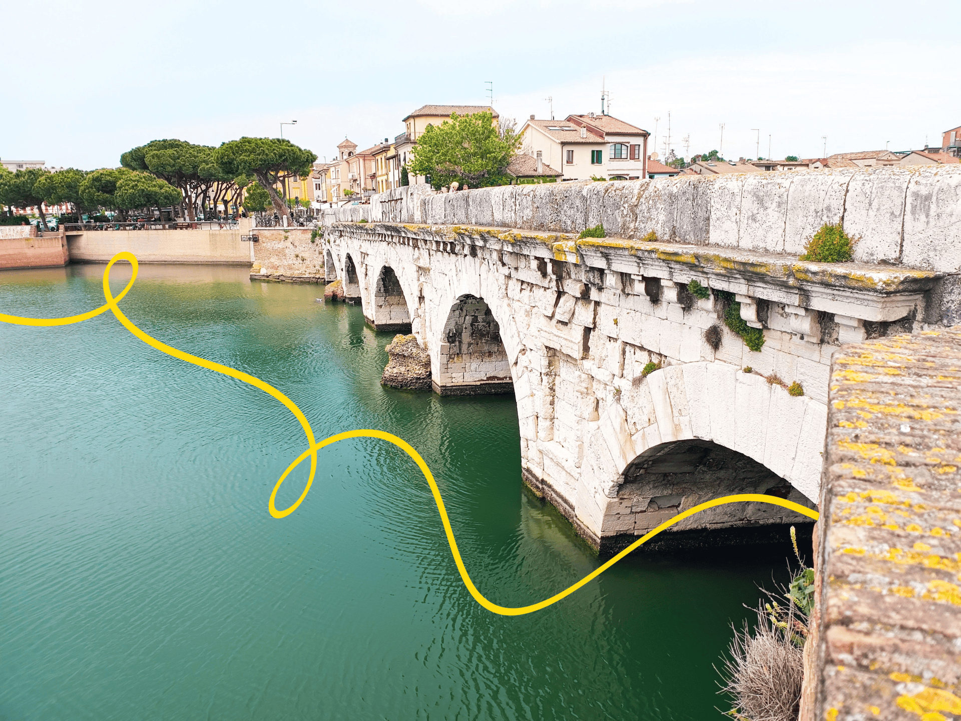 Photograph of an ancient stone bridge with multiple arches spanning a calm green river.
