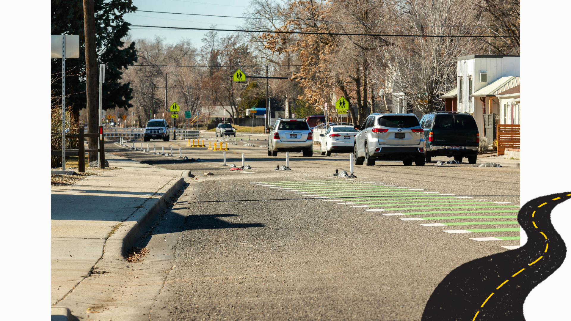 Photograph of a residential street with several cars driving and parked along the road, featuring a pedestrian crosswalk marked with green and white stripes. Trees with autumn foliage and pedestrian crossing signs are visible in the background.