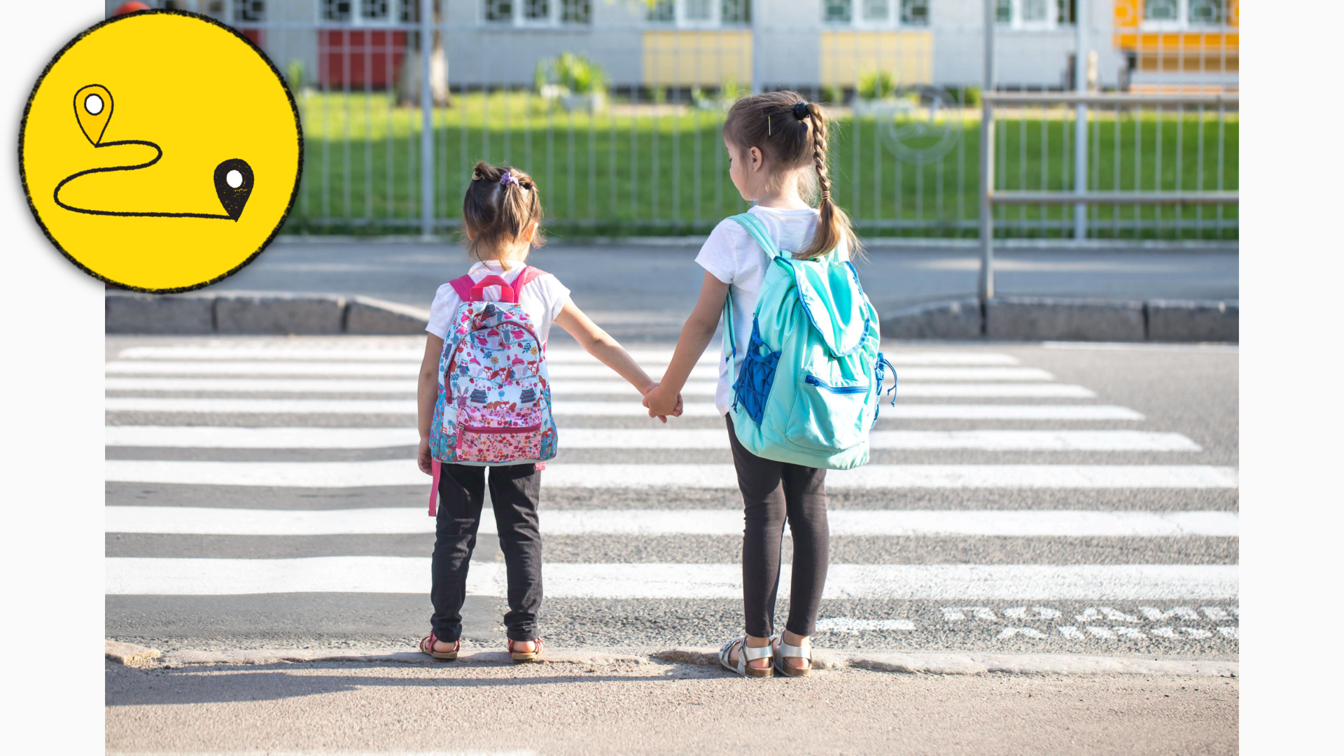 Two girls hold hands in front of a school crosswalk.