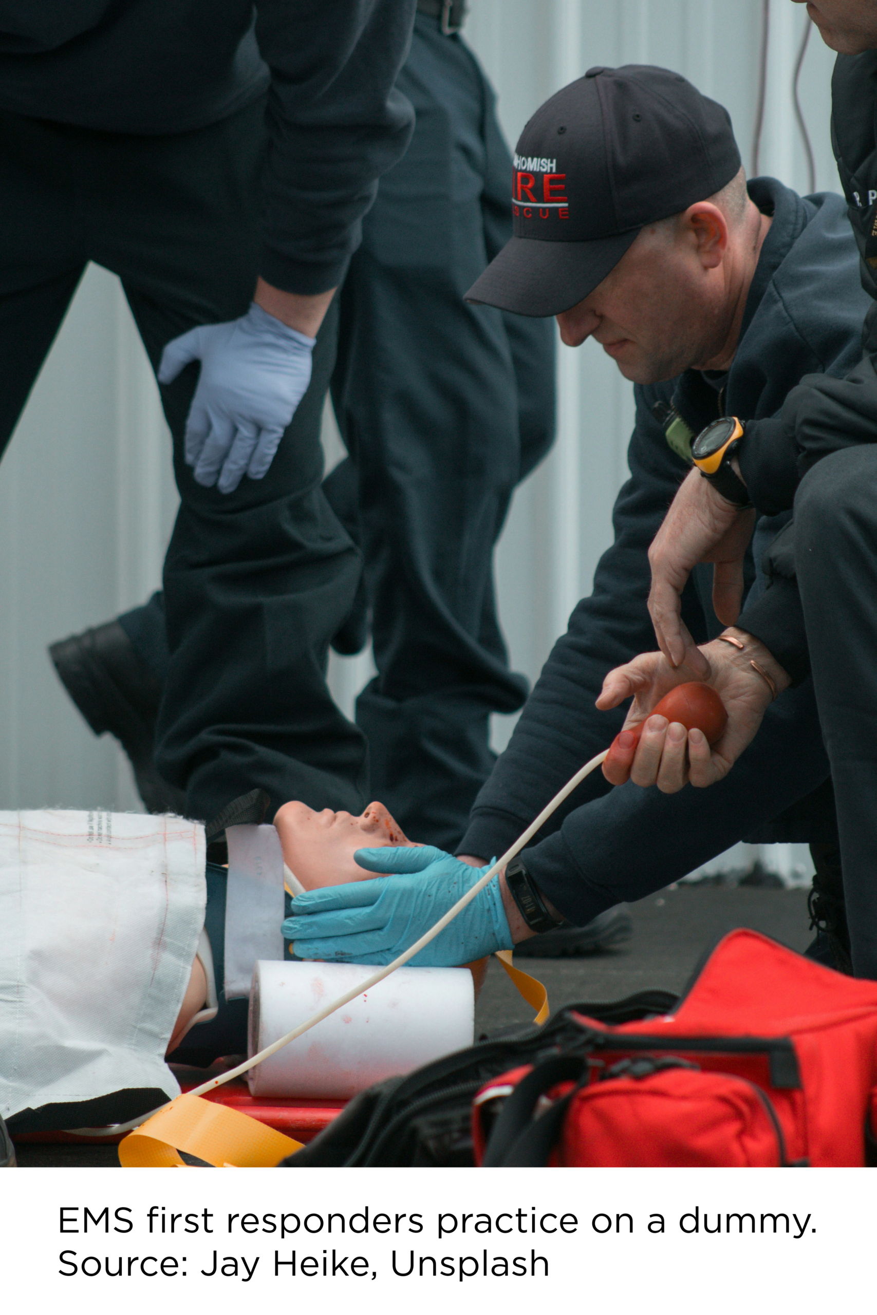 Photograph showing emergency responders conducting hands-on medical treatment during a rescue or first-aid training exercise. Caption reads: EMS first responders practice on a dummy. Source: Jay Heike, Unsplash